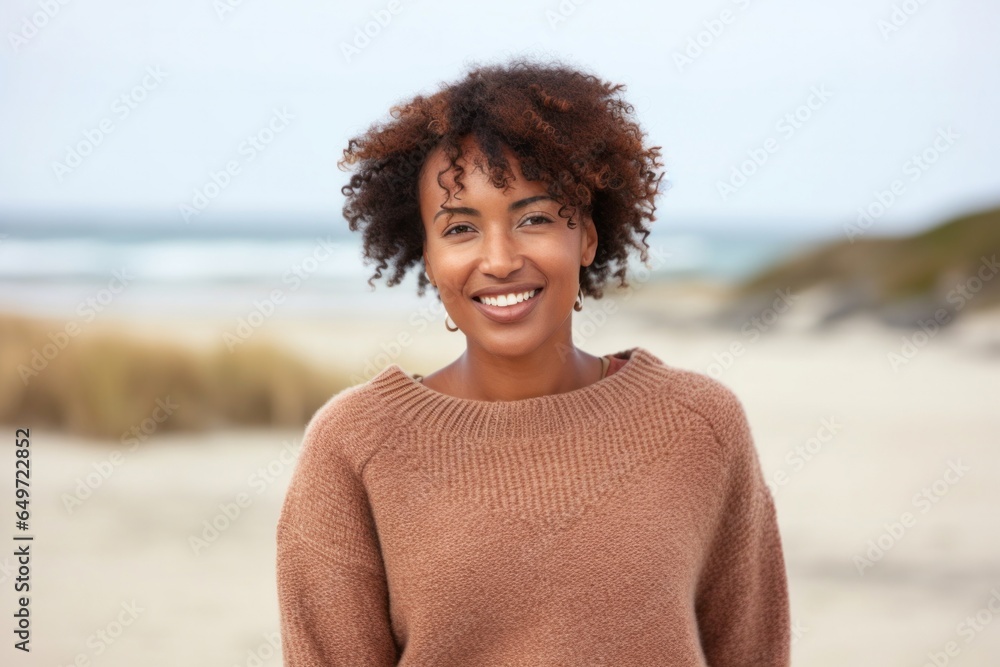 Portrait of a confident Kenyan woman in her 30s wearing a cozy sweater against a beach background Portrait of a confident Kenyan woman in her 30s wearing a cozy sweater against a beach background