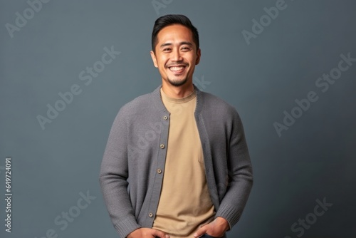 medium shot portrait of a happy Filipino man in his 30s wearing a chic cardigan against a minimalist or empty room background
