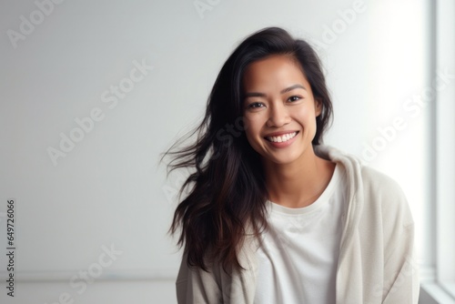 portrait of a happy Filipino woman in her 30s wearing a cozy sweater against a minimalist or empty room background
