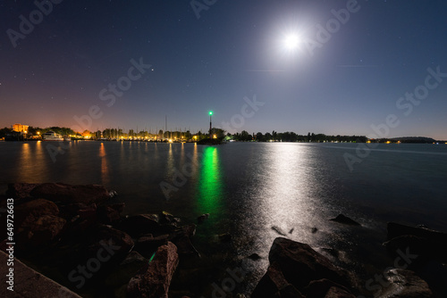 Balaton lake in Hungary, night view. Scenic landscape with yacht marine, lighthouse, dark blue sky with stars and moon, calm water with reflection, outdoor travel background photo