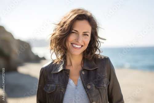 portrait of a happy Israeli woman in her 40s wearing a denim jacket against a beach background © Leon Waltz