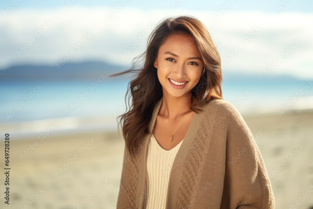 medium shot portrait of a Filipino woman in her 20s wearing a chic cardigan against a beach background