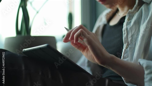 Woman artist drawing on tablet. Creative girl holding notepad with digital pencil in hands and working remotely from home. Freelancer using computer to create art sitting near window