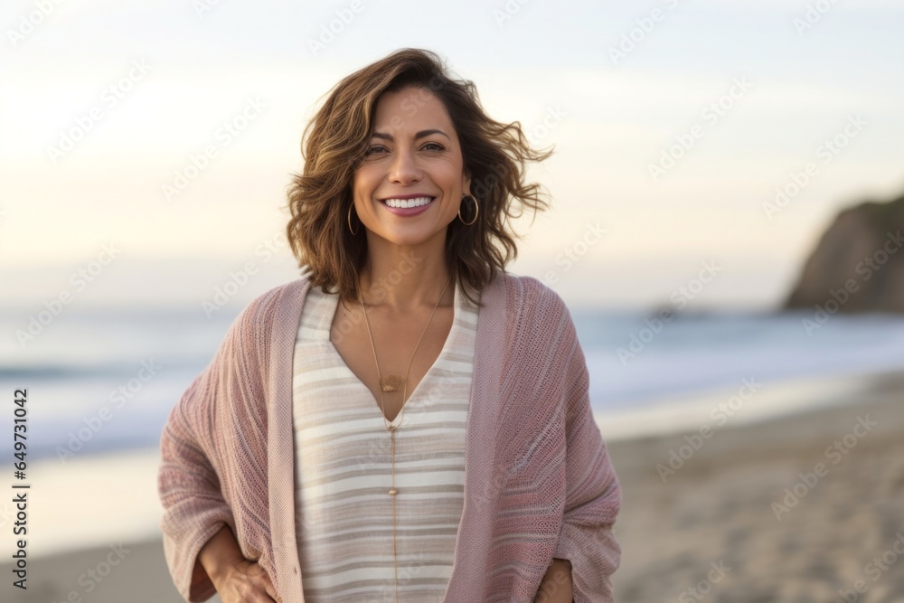 medium shot portrait of a Mexican woman in her 40s wearing a chic cardigan against a beach background