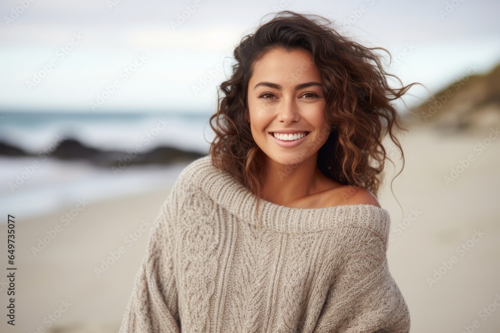 portrait of a Mexican woman in her 20s wearing a cozy sweater against a beach background