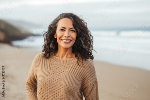 portrait of a Mexican woman in her 50s wearing a cozy sweater against a beach background