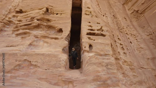 Woman exiting a large cave carved into sandstone rock.