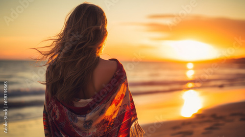 Fototapeta Naklejka Na Ścianę i Meble -  Young beautiful woman looking at sunset on the beach with a shawl on her shoulders on a fresh evening