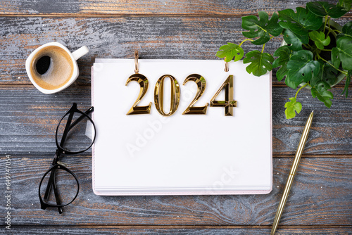 New year resolutions 2024 on desk. 2024 goals list with notebook, coffee cup, plant on wooden table. Resolutions, plan, goals, action, checklist, idea concept. New Year 2024 resolutions, copy space