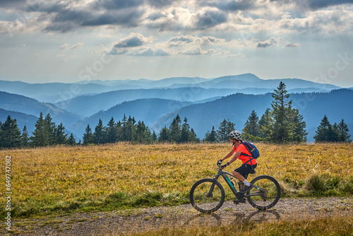 nice senior woman on her electric mountain bike cycling on Feldberg summit with stunning view over the Black Forest mountains and valleys, Baden-Wuerttemberg Germany photo