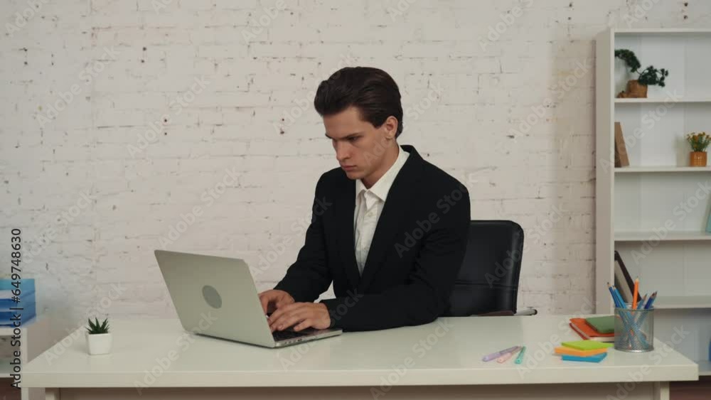 Medium video of a young man sitting at the table, working on a laptop, then massaging his neck that is hurting after a long day, shift. Medium video of a young man sitting at the table, working on a laptop, then massaging his neck that is hurting after a long day, shift.