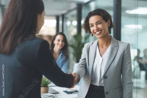 two businesswomen shake hands in agreement and cooperation, in an office with a diverse and inclusive staff, empowering women in the workplace and female leadership in professional environments. photo