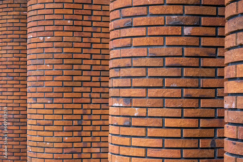 Four columns lined up in a row and faced with red clinker brick. Brick walls of brown brick. Brick wall as background.