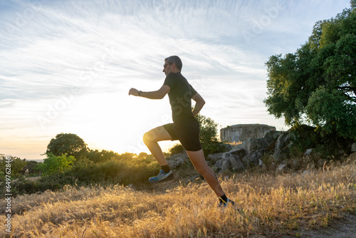 Middle-aged trail runner with gray hair leaping at sunset.