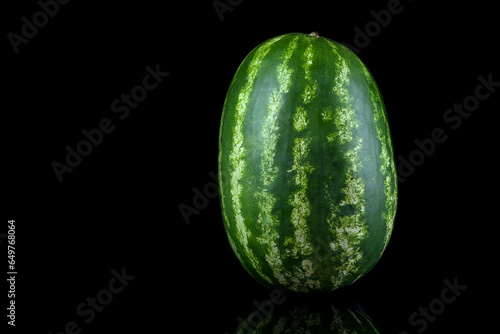 A whole big watermelon on a black table background. Green, hard and striped watermelon.