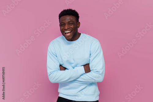 cheerful african american man in blue sweater laughing on pink isolated background © Богдан Маліцький