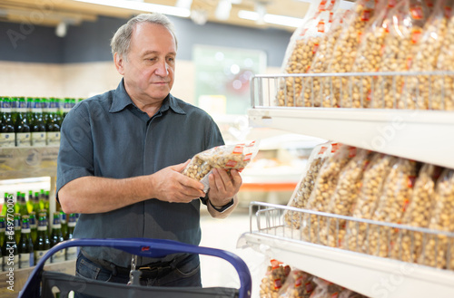 Elderly man carefully reads the date on the package of pistachios