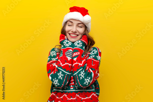 girl in warm Christmas sweater and santa claus hat smiles on yellow isolated background