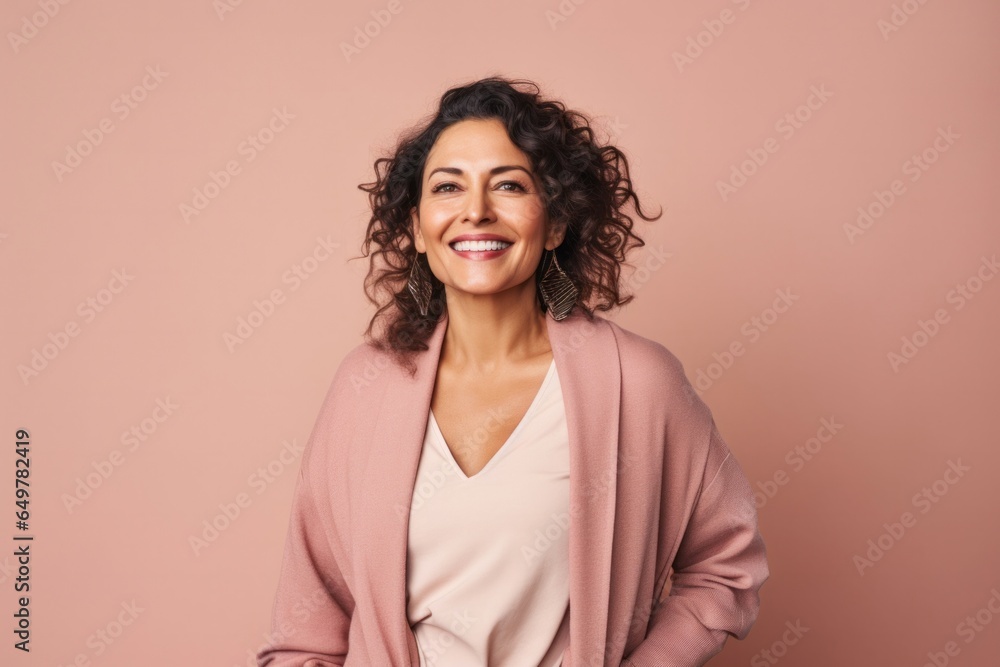 Happy woman with curly brown hair smiling at camera in indoor studio with colored background