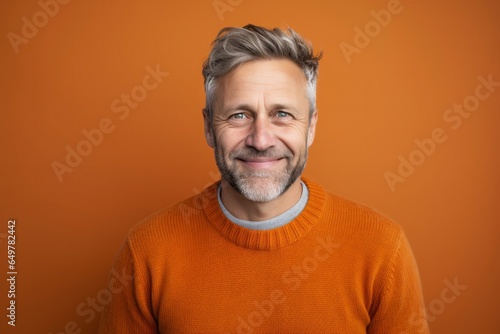 Smiling senior man with gray hair in sweater against orange background