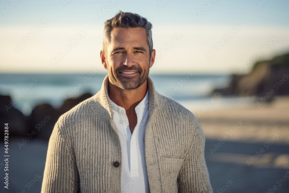Happy smiling man with beard standing on beach, looking at camera