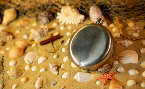 Steel flask on sand among shells and stones. (ID: 649786233)