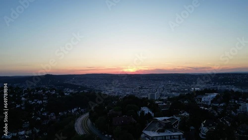 In diesem atemberaubenden Drohnenshot fliegt die Kamera über Stuttgart, während der Himmel sich in ein magisches Lila verwandelt und die Sonne am Horizont untergeht. photo