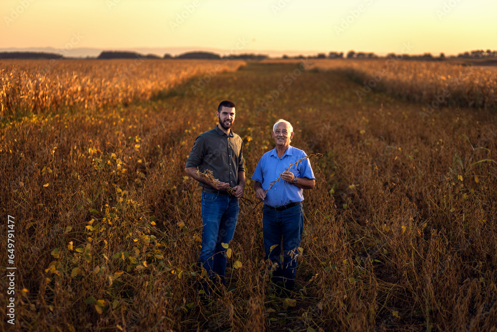 Portrait of two farmers standing in soy field looking at camera.