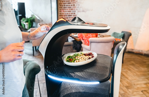 Robot waiter serve food at modern restaurant table.Offering innovation futuristic high-tech automated dining experience.Bringing,delivery automation order to customer.Digital robotic AI smart service