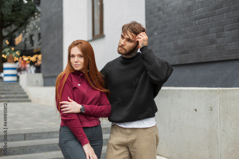 Cool fashion couple hipster man and redhead woman in fashionable hoodie on the street