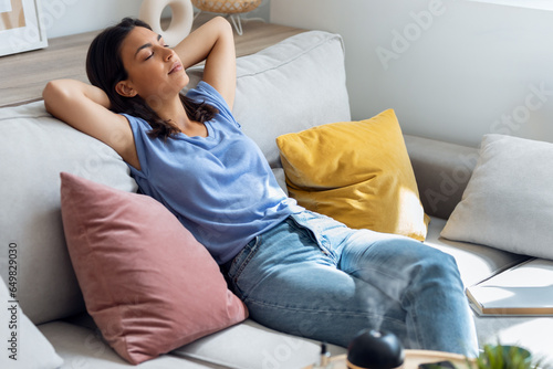 Beautiful woman relaxing on a coach while essential oil aroma diffuser humidifier the air in living room at home photo