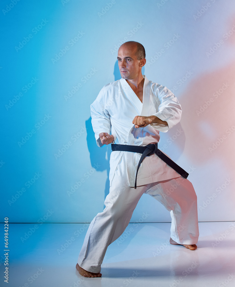Trainer with black belt training formal exercises on color background with blue and pink tint Trainer with black belt training formal exercises on color background with blue and pink tint