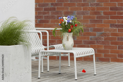 Wild flower bouquet (Cornflowers, chamomiles wheat and poppies) in terracotta vase on summer terrace. Wildflower and grass varieties.