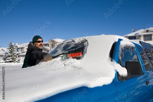 Man Brushing Snow Off A Vehicle's Windshield; Calgary, Alberta, Canada
