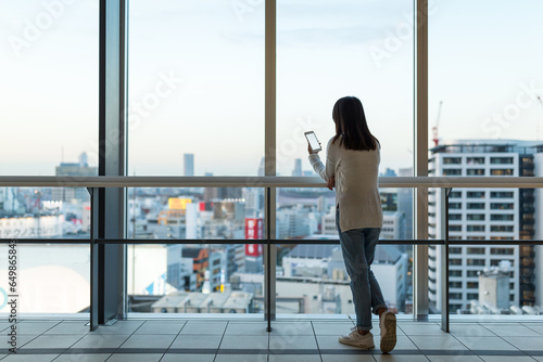 Woman use mobile phone over the big window inside business office tower