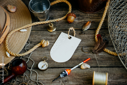 Fishing theme. Label with hooks, bucket, fishing buoy, compass and fish string on wooden background. Free space