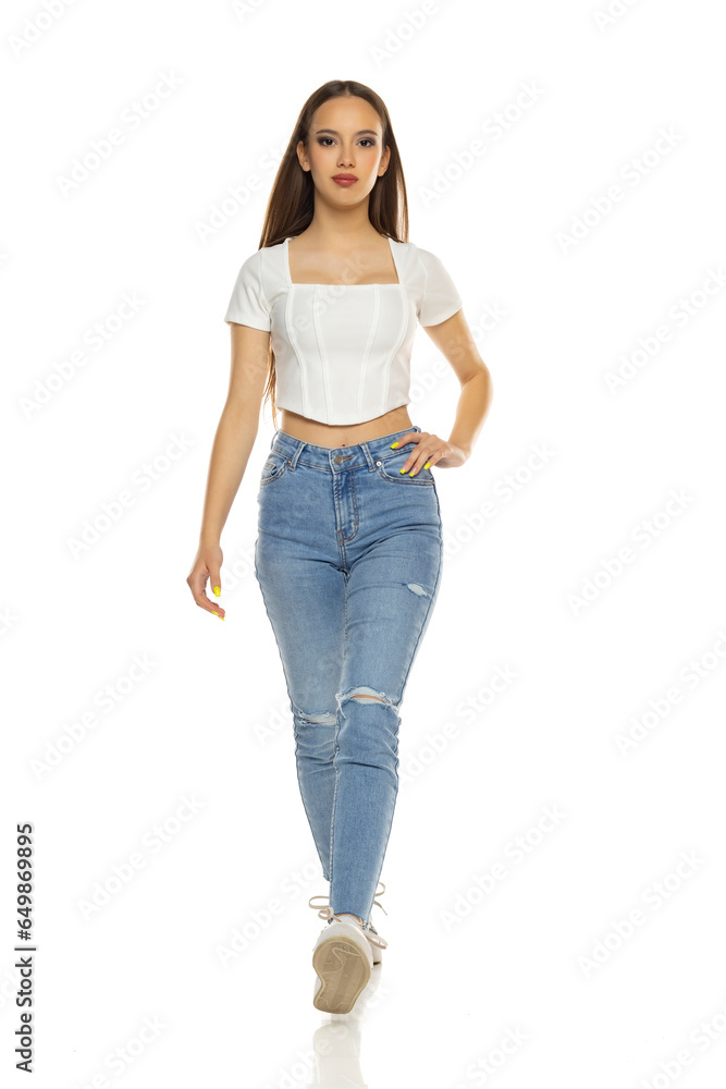 Young woman in white shirt, blue jeans and sneakers walk on a white background Young woman in white shirt, blue jeans and sneakers walk on a white background