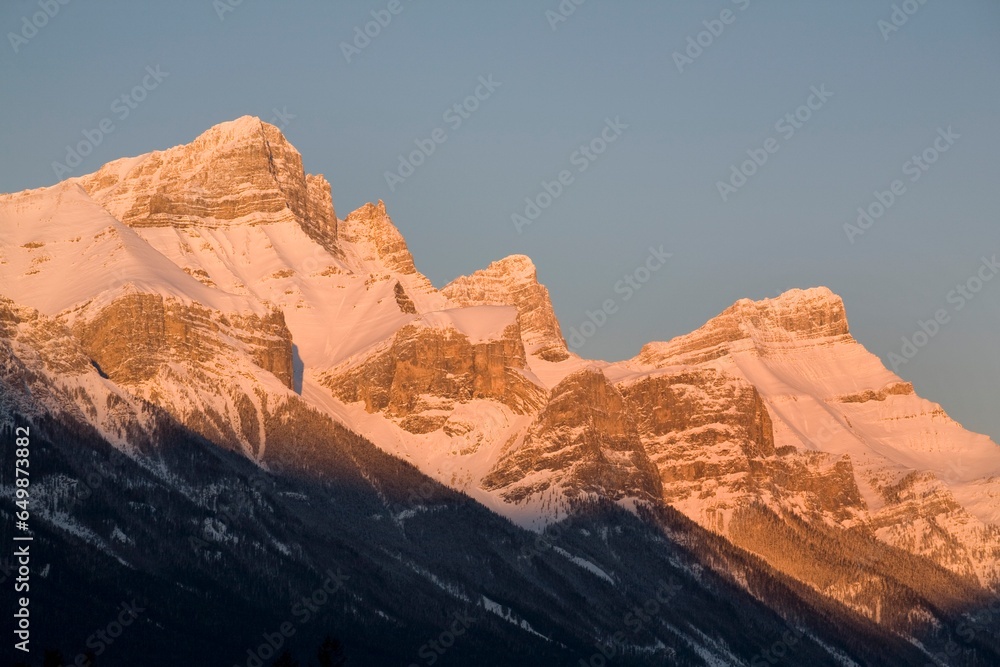 Sunlight Shining On Snow Covered Mountains Against A Blue Sky; Canmore, Alberta, Canada