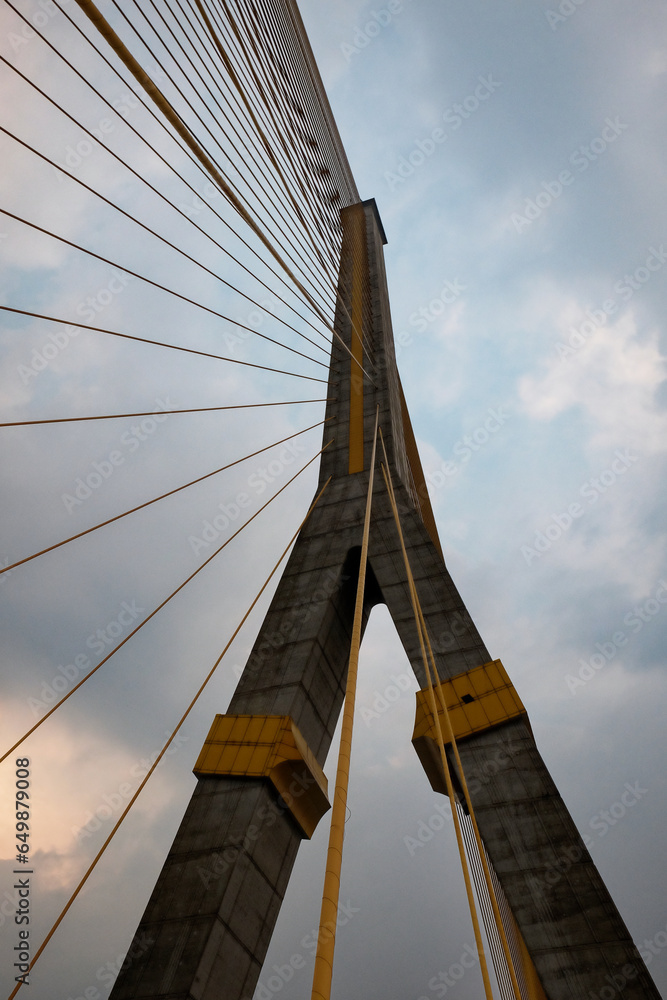 Obraz premium A towering suspension bridge, with concrete pillars and steel cables, cloudy sky.