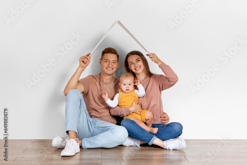 Family Housing. Happy Parents With Infant Baby Sitting Under Symbolic Cardboard Roof © Prostock-studio