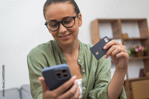 Efficacious e-shopping: A cheerful woman adeptly pays via her phone, ensuring a seamless online shopping experience. 