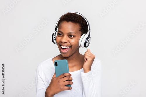 Beautiful dark skinned african girl singing at cell phone microphone satnding over white background in studio isolated smiling having fun wearing modern new headphones earphones headset photo