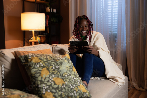 Εκτύπωση καμβά Cheerful young afro american woman sitting in the living room holding tablet in