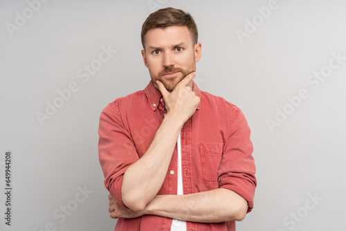 Pensive puzzled thoughtful man looking at camera touching chin isolated background. Embarrassed guy feeling confusion solves problems, struggling with choice. Haughty caucasian male pondering idea.