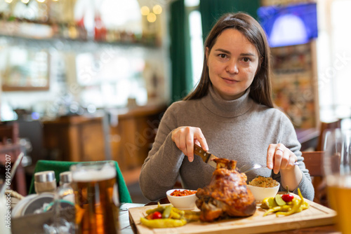 Canvas Print Female traveler tasting fried pork ham knuckle traditionally served with stewed cabbage, pickled vegetables, various sauces and beer in cafe in Vienna