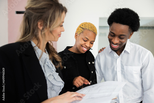Blonde real estate agent explains the energy-saving features of the house as African American dark skinned couple looks on with keen interest impressed by the eco-friendly design happy family concept