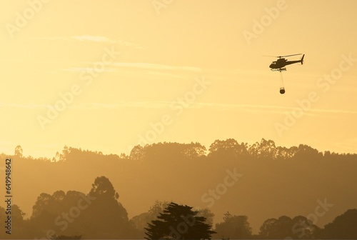 Emergency helicopter, firefighters, with the last hours of the setting sun heading to a fire in the mountains.