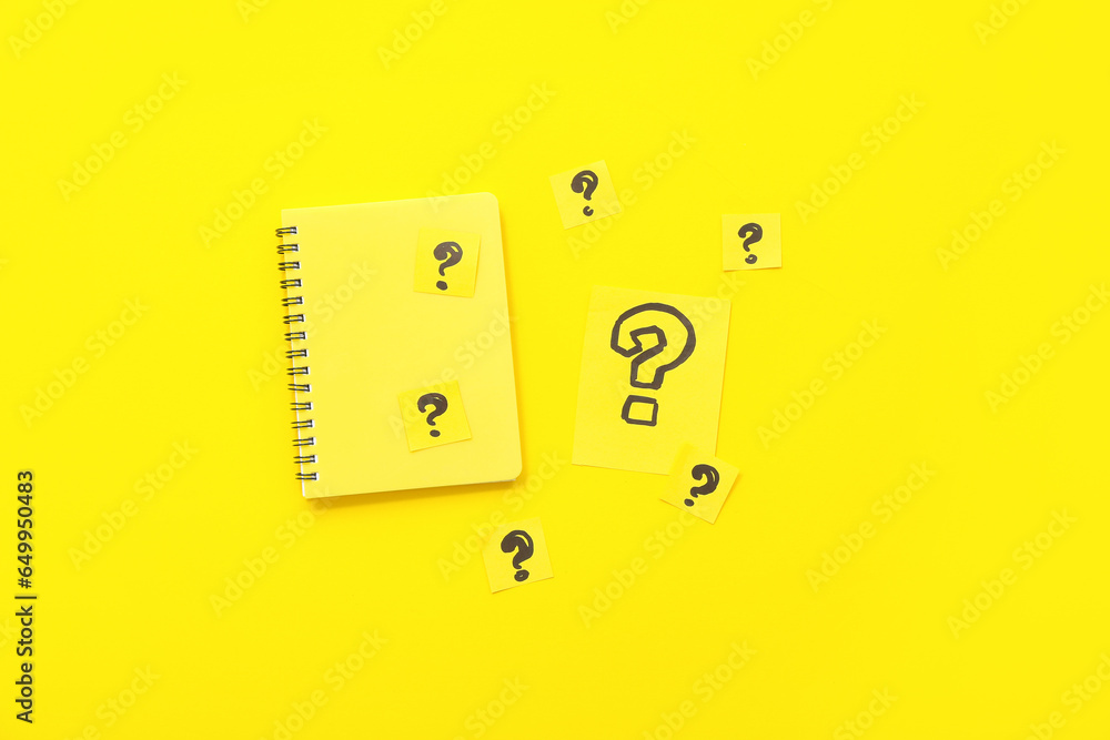 Notebook with paper question marks on yellow background Notebook with paper question marks on yellow background