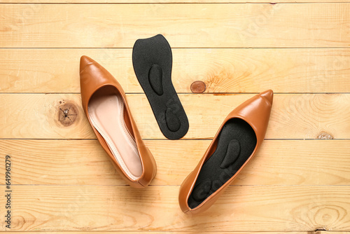 Pair of stylish female shoes and orthopedic insoles on wooden background