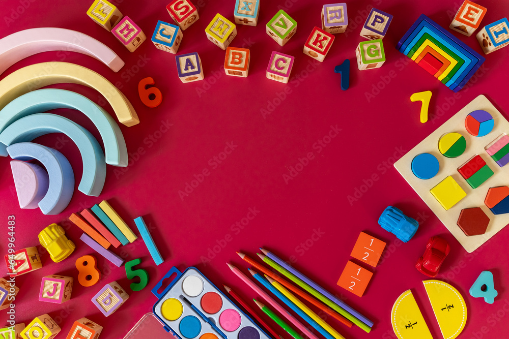 Wooden kids toys on red paper. Educational toys blocks, pyramid, pencils, numbers. Toys for kindergarten, preschool or daycare. Copy space for text. Top view Wooden kids toys on red paper. Educational toys blocks, pyramid, pencils, numbers. Toys for kindergarten, preschool or daycare. Copy space for text. Top view
